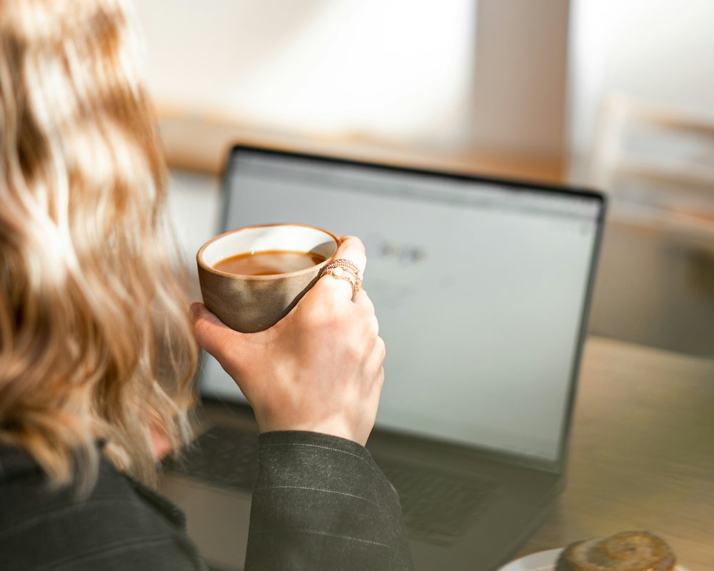 Pessoa com café em frente ao notebook